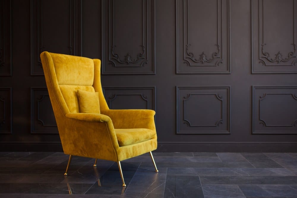 Stylish yellow velvet chair against a dark gray wall.